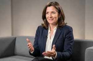 Femme journaliste française en interview télévisée dans un studio moderne, blazer marine et chemisier blanc, expression assurée